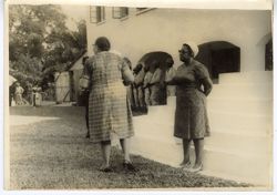 Two women stand in front of steps with military officials of to side