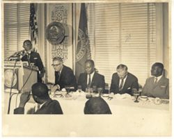 President William V. S. Tubman stands at podium while others are seated at conference table