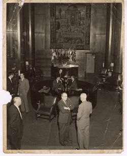 Dignitaries talk in a hall with several flags in the background