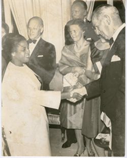 Man shakes woman's hand with small gathering in background