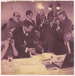 Man hands object to President William V. S. Tubman while press and guests laugh