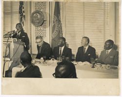 President William V. S. Tubman stands at podium while others are seated at conference table