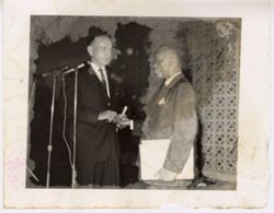 Two men stand together in front of microphone