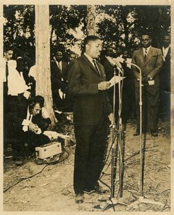 Man speaks in microphones with crowd gathered around
