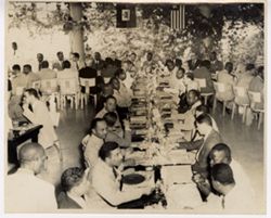 Dignitaries sit at a meal with the Haitian and Liberian flags hanging in the background