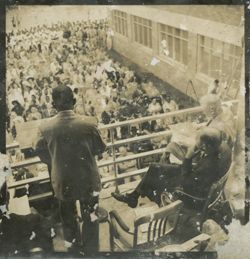 President Tubman addresses a crowd from a balcony, dignitaries are seated beside him