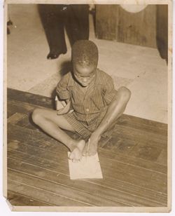 Armless boy writing with two toes of  left foot.