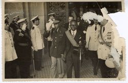 President William V. S. Tubman in formal attire leaves building with military officials saluting