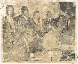 President William V. S. Tubman sits at table and signs document with men standing behind
