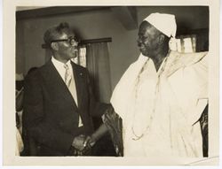 Ambassador C. T. O. King and man in ceremonial garb exchange greeting