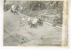 Men in uniform on motorcycles next to men standing in driveway