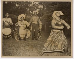 Woman dressed in traditional dress dancing to music played by men on drums