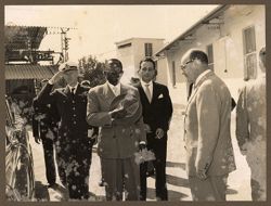 President Tubman holds his hat over his heart, a military officer salutes in the background