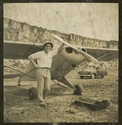 Man in a pith helmet stands next to a small airplane