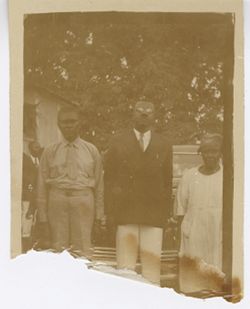 Two men and a woman pose outside of the home of Mr. Wilmot F. Talm