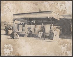 A group sits under an awning, portraits of President Tubman and othe leaders sit in front of them