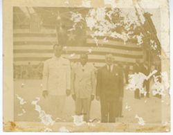 President William V. S. Tubman and two others stand in front of large flag