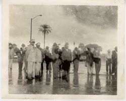 Officials and military officials stand outside in the rain