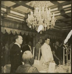 Men stand at formal dinner table underneath chandelier