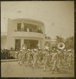 Military band march in parade past crowds in front of Executive Pavilion