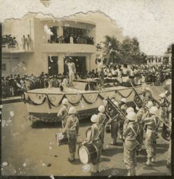 Float drives down street past military band during parade outside Executive Pavilion