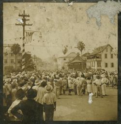 Crowd gathers in the street, looking down the road away from the camera