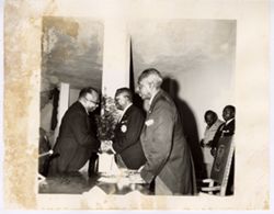 President William V. S. Tubman leans over table and shakes hands with man