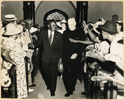 President William V. S. Tubman greets church attendees while walking with priest during visit to parish of St. Catherine, Clarendon and May Pen