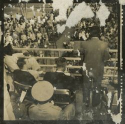 President Tubman stands on a balcony facing a crowd, digitaries and military officers are seated around him