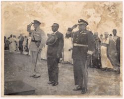 Military officials salute while President William V. S. Tubman holds his hat over his heart