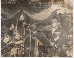 President William V. S. Tubman in formal attire speaks at podium surrounded by microphones and Liberian flags