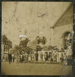 People stand on the sidewalk looking toward a building, a Liberian flag waves in the backgound
