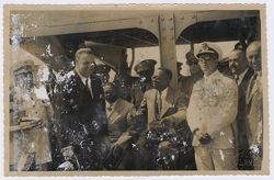 President Tubman smiles and talks to a dignitary while surrounded by military officials