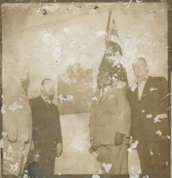 Group of men stand by Harvey S. Firestone plaque and Liberian flag