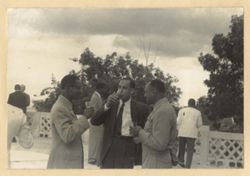 Three men stand together with drink in hand