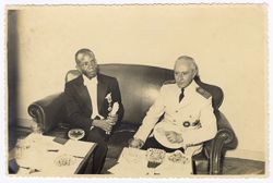 Two men in decorated dress sit together on couch