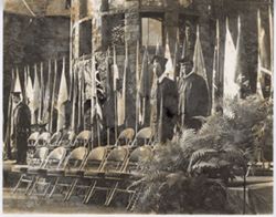Men in commencement attire stand on stage outdoors