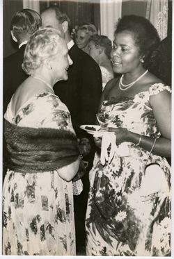 Wife of Swedish banker and another woman in formal dress talk at cocktail party