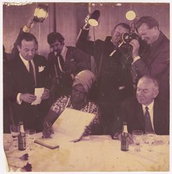 Woman signs book while the press documents occasion behind her