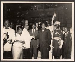 Dignitaries pose with a soldier, a camera man films the scene from behind the group