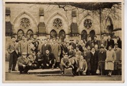 Group poses for portrait outside with large windows in background
