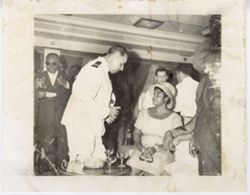 Military official talks to woman during during an event, President William V. S. Tubman in background