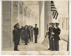 Men stand before soldiers in uniform carrying American flag