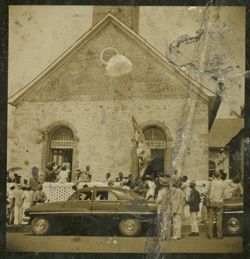People stand on the sidewalk looking towards a building, possibly a church