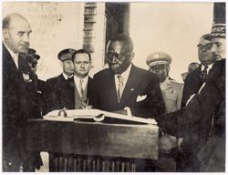 President William V. S. Tubman signs book on podium with other digitaries in background