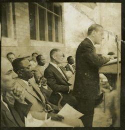 Dignitary speaks into a microphone with President Tubman officials seated behind him