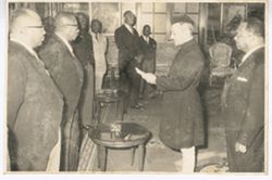 Man in traditional dress reads from paper in front of President William V. S. Tubman, Vice President Tolbert, and others