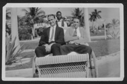 Man identified as Hue (left) and unidentified man in a rickshaw, with an unidentified man behind them, surrounded by palm trees.