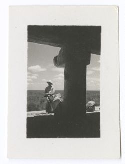 Item 1006. Unidentified man from Items 1005-1005b above, seen through doorway of temple atop atop the Castillo. He is seated on a stone, holding a camera across his knees.