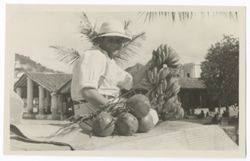 Item 0311. Eisenstein seated on the steps, holding up bananas, other fruit beside him, buildings in the background.
